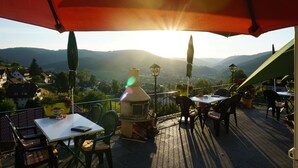 An outdoor patio with tables and chairs, a pizza oven, and a view of the surrounding landscape. - Pension Talblick (Baiersbronn)