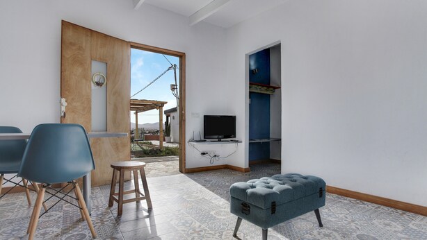 Een kamer met een televisie, een blauwe stoel, een houten deur en een vloer met een patroon.
