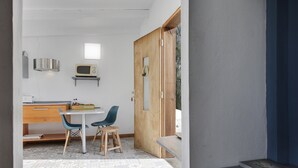 Een compacte keuken met een magnetron, houten kastjes en een kleine eethoek met stoelen.