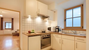 A modern kitchen with a stove, microwave, and sink, wooden cabinets, and a window with blinds. - Holiday Apartment “Rafaser - Albina” with Mountain View & Wi-Fi (Feldthurns)