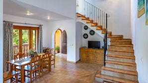 Ein Essbereich mit Holztisch und Stühlen, eine Treppe mit Holzstufen und Metallgeländern sowie ein Fernseher auf einer Holzkommode.
