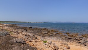 Eine felsige Küstenlinie mit klarem, blauem Wasser und Bergen im Hintergrund.