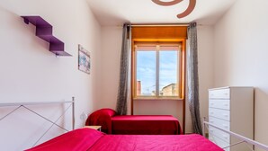 A bedroom with two beds, a window with curtains, a white dresser, and a purple staircase. - Apartment near the sea - Appartamento Torre Lapillo (torre lapillo)