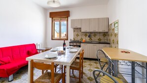 A compact living space with a dining table, red sofa, kitchen area, and a window with a view. - Apartment near the sea - Appartamento Torre Lapillo (torre lapillo)