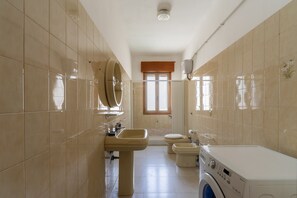 A bathroom with a washing machine, a sink, a toilet, and a window.