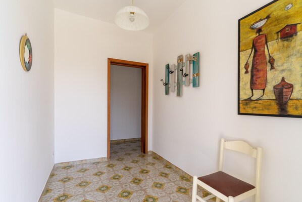 Un pasillo con una puerta, una silla, un cuadro y un adorno en la pared.