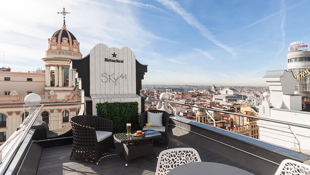 A rooftop terrace with outdoor seating, a Heineken sign, and a view of the cityscape. - Hostal Juliette & Coworking (Madrid)
