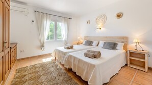 Et hotelværelse med to senge, et træskab, et vindue med gardiner, en vægmonteret lampe og et tæppe.