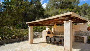 En udendørs patio med flisebelagte gulve, en pergola og en stenvæg.