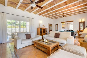 A spacious living room with a pool table, white sofas, wooden coffee table, and a ceiling fan.