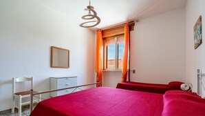 A bedroom with a bed, a chair, a desk, a window with curtains, and a hanging light fixture. - Close to the beach with courtyard - Apartment Lapillo (torre lapillo)