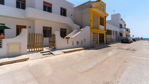 A coastal street with white buildings, a yellow corner building, and parked cars. - Close to the beach with courtyard - Apartment Lapillo (torre lapillo)
