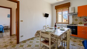A dining area with a table set for two, a television mounted on the wall, and a kitchen with orange cabinets. - Close to the beach with courtyard - Apartment Lapillo (torre lapillo)