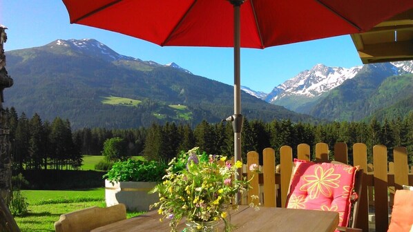 A wooden deck with a table and chairs, a red umbrella, and a vase of flowers.