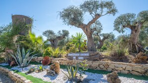 Un jardin avec un mur de pierre, de grands arbres et un panneau indiquant la présence d’hébergements en milieu rural.