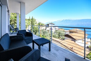 Un balcon agrémenté de meubles en osier, une vue sur un paysage montagneux et un plan d’eau.