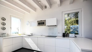 Una cocina moderna con armarios blancos, horno integrado y ventana con vista a la vegetación.