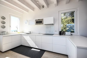 A modern kitchen with white cabinetry, a built-in oven, and a window with a view of greenery.