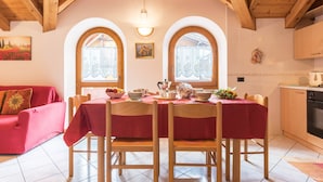 A dining area with a table set for four, wooden chairs, a red tablecloth, and two arched windows. - Holiday Apartment "Bamby - Vioz" with Balcony, Garden & Mountain View (Cogolo di Pejo)
