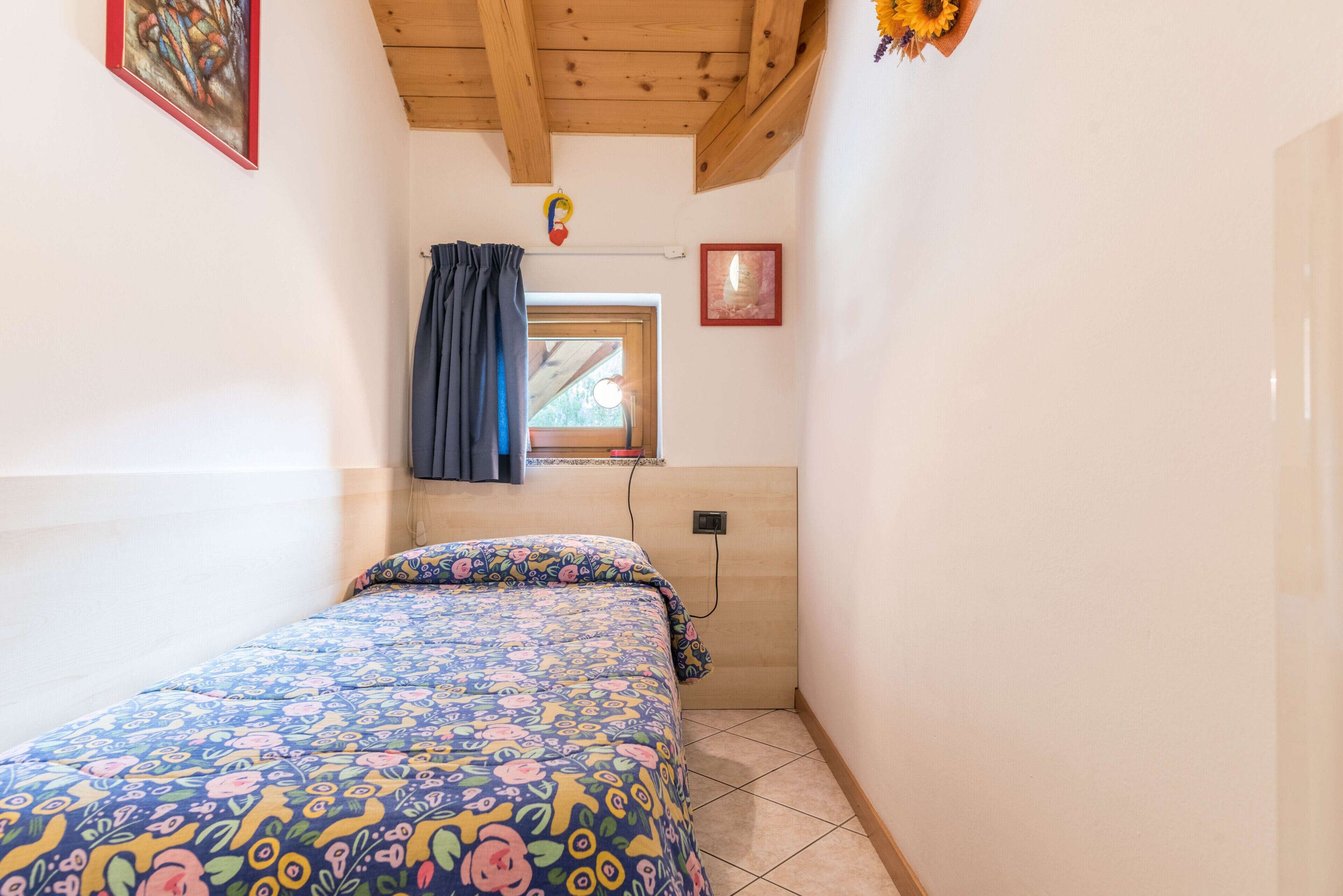 Un dormitorio pequeño con una cama, una ventana con cortinas, una lámpara de pared y un cuadro enmarcado.
