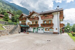 Un bâtiment de style chalet traditionnel, doté d’un escalier en pierre, de balcons en bois et d’une allée gravillonnée.