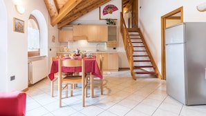 A kitchen with wooden cabinets, a dining table with chairs, a refrigerator, and a wooden staircase. - Holiday Apartment "Bamby - Vioz" with Balcony, Garden & Mountain View (Cogolo di Pejo)