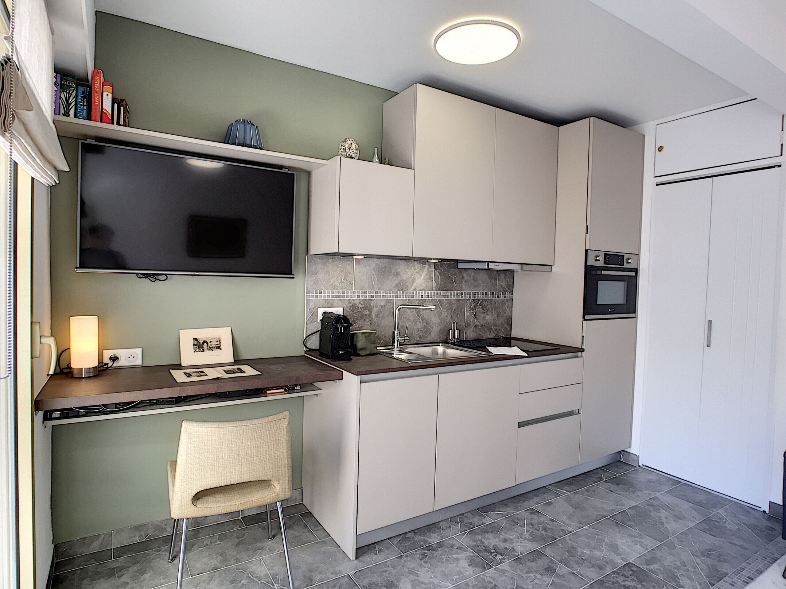 A modern kitchen with a flat-screen TV, a coffee machine, and a sink.