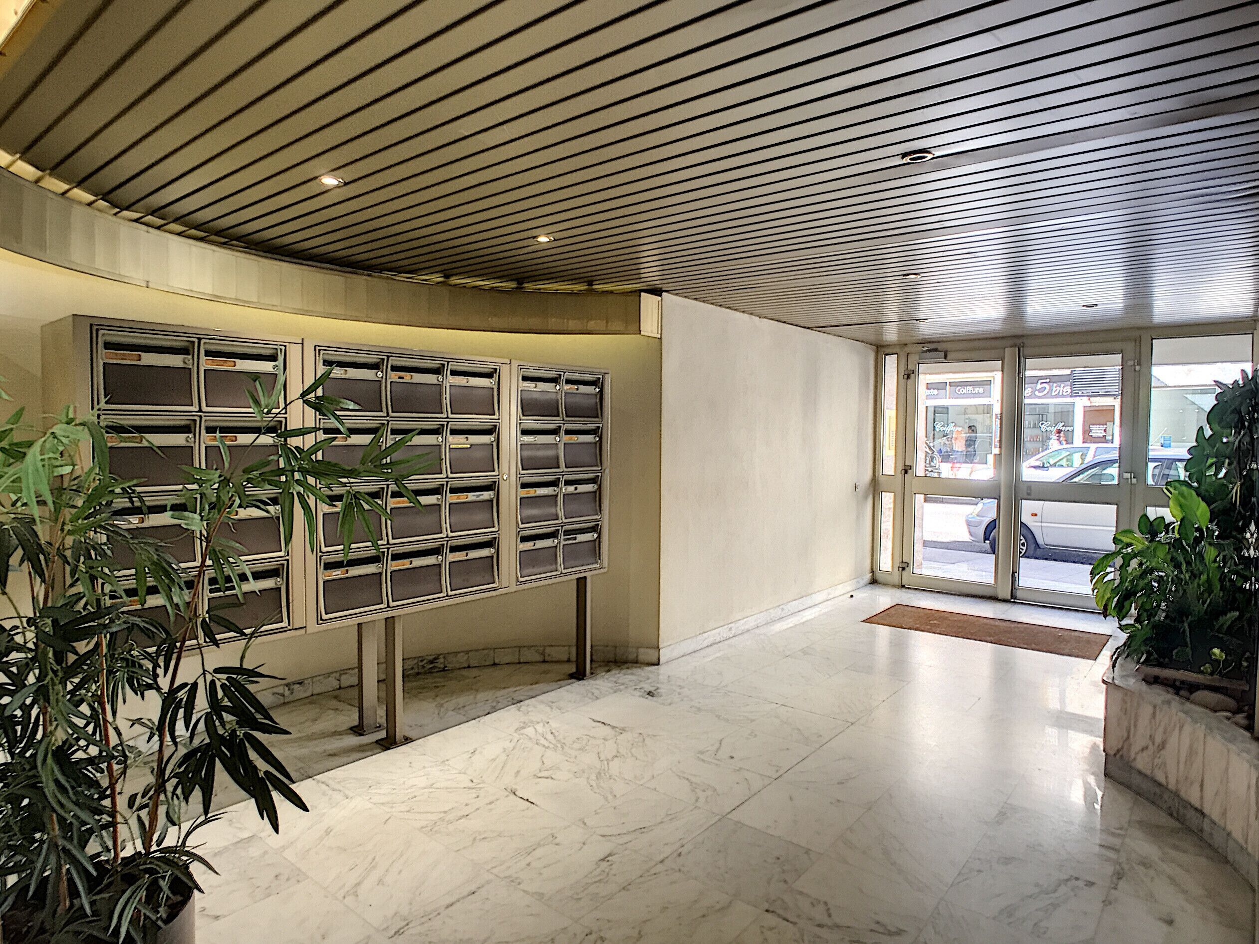 A modern lobby with a marble floor, a metal bulletin board, and potted plants.