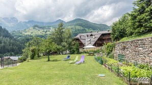 A mountain lodge with a stone wall, a grassy lawn, and a view of the surrounding mountains.