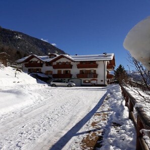 Een chalet met twee verdiepingen, een oprit bedekt met sneeuw en een berg op de achtergrond.