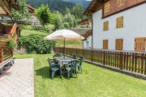 Een terras met een tafel, stoelen, een witte parasol en een houten hek.