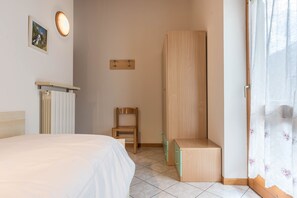 Een slaapkamer met een bed, een stoel, een kledingkast, een radiator en een schilderij aan de muur.