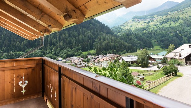 A wooden balcony with a view of a village and mountains.
