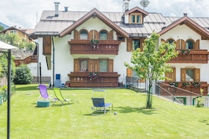Una cabaña tradicional con techo inclinado, balcones de madera y un césped cuidado con mobiliario exterior.
