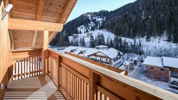 A wooden balcony with a view of snow-covered houses and a forested mountain. - Idyllic Apartment "Kronplatz" with Balcony, Garden and Wi-Fi (San Martino in Badia)