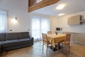 Une cuisine moderne avec des meubles blancs, une table à manger avec des chaises et un canapé gris dans une pièce lumineuse dotée de grandes fenêtres.