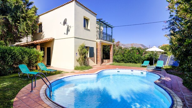 Ein zweistöckiges Haus mit Pool, Balkon und einer Terrasse mit Stühlen und Sonnenschirm.