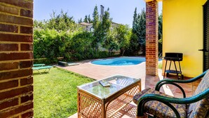 Ein Garten mit Swimmingpool, Glastisch, Korbstühlen und einer Backsteinmauer.