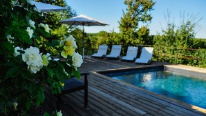 Une terrasse en bois avec une piscine, des chaises longues blanches et des parasols.