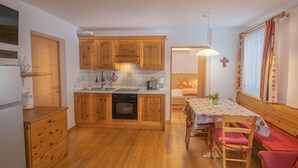 A compact kitchen with wooden cabinets, a dishwasher, and a dining area with a table and benches. - Cozy 'Apartment Enzian' with Mountain View, Wi-Fi, Garden & Terrace (Sand in Taufers)