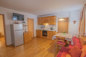 Une cuisine de taille réduite, dotée de meubles en bois, d’un réfrigérateur et d’un coin repas avec une table et des chaises.