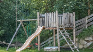 Eine hölzerne Spielkonstruktion mit Rutsche und Kletterelementen auf einer Rasenfläche.