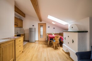 Une cuisine avec des meubles de rangement en bois, une table à manger avec des chaises, un réfrigérateur et une lucarne.
