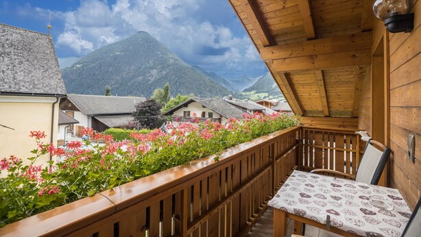 Ein Holzbalkon mit Tisch und Stühlen mit Blick auf einen Berg und ein Dorf.