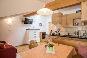 Une cuisine de taille réduite, dotée de meubles en bois, d’une table à manger et d’un téléviseur fixé au mur.