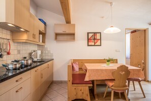 Une cuisine avec des meubles de rangement en bois, un plan de travail sur lequel sont posées des casseroles, un banc et une table avec des chaises.