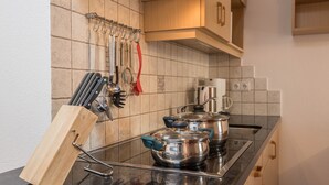 Eine Küche mit Herd, Töpfen, einem Messerblock und hängendem Kochgeschirr.