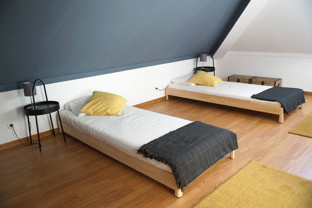 A small, modern bedroom with two single beds, a bedside table, a lamp, and a wooden floor.