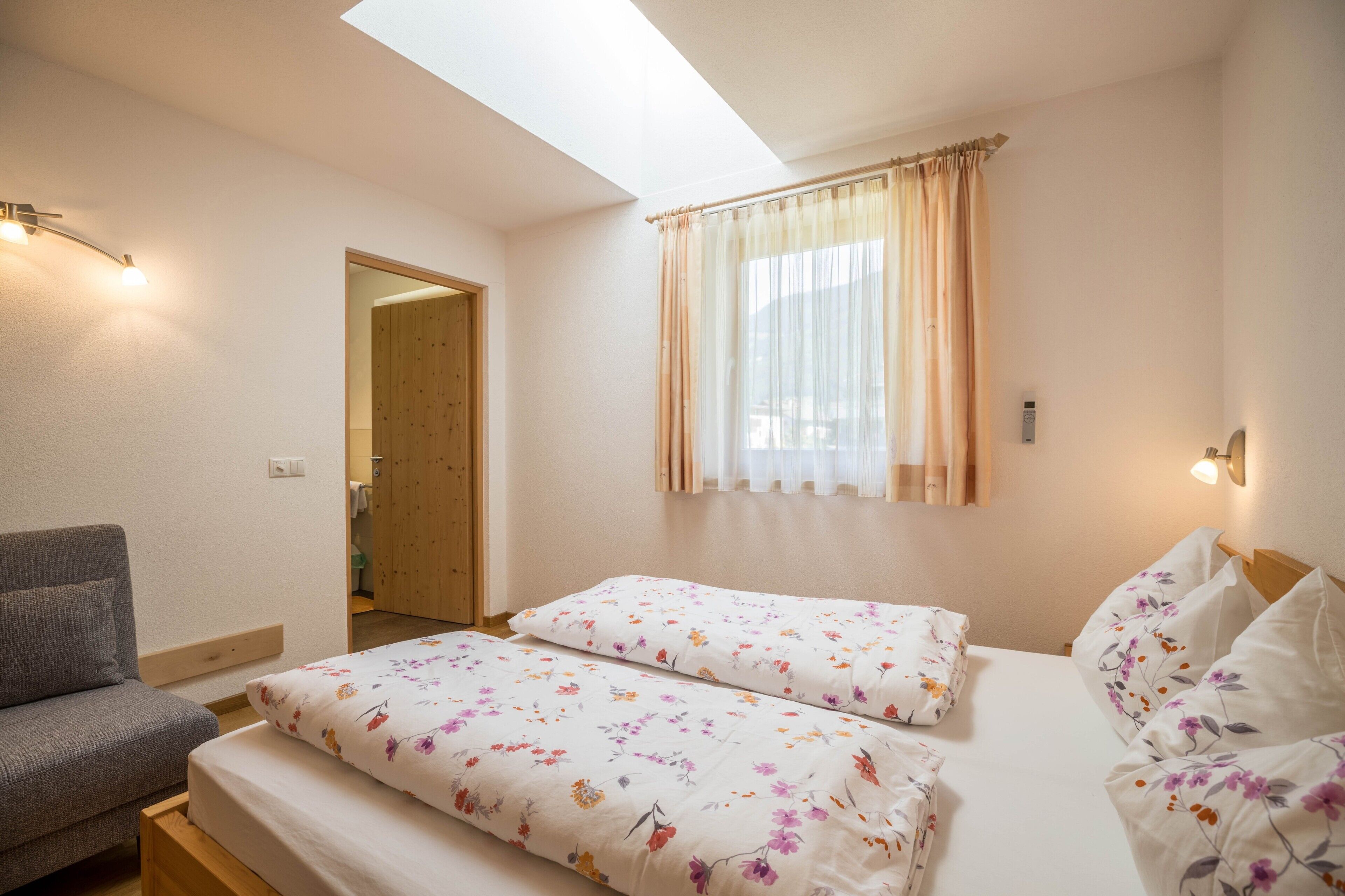 Ein Schlafzimmer mit zwei Betten, einem Schlafsofa, einem Oberlicht und einem Fenster mit Vorhängen.