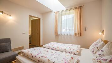 Ein Schlafzimmer mit zwei Betten, einem Schlafsofa, einem Oberlicht und einem Fenster mit Vorhängen.
